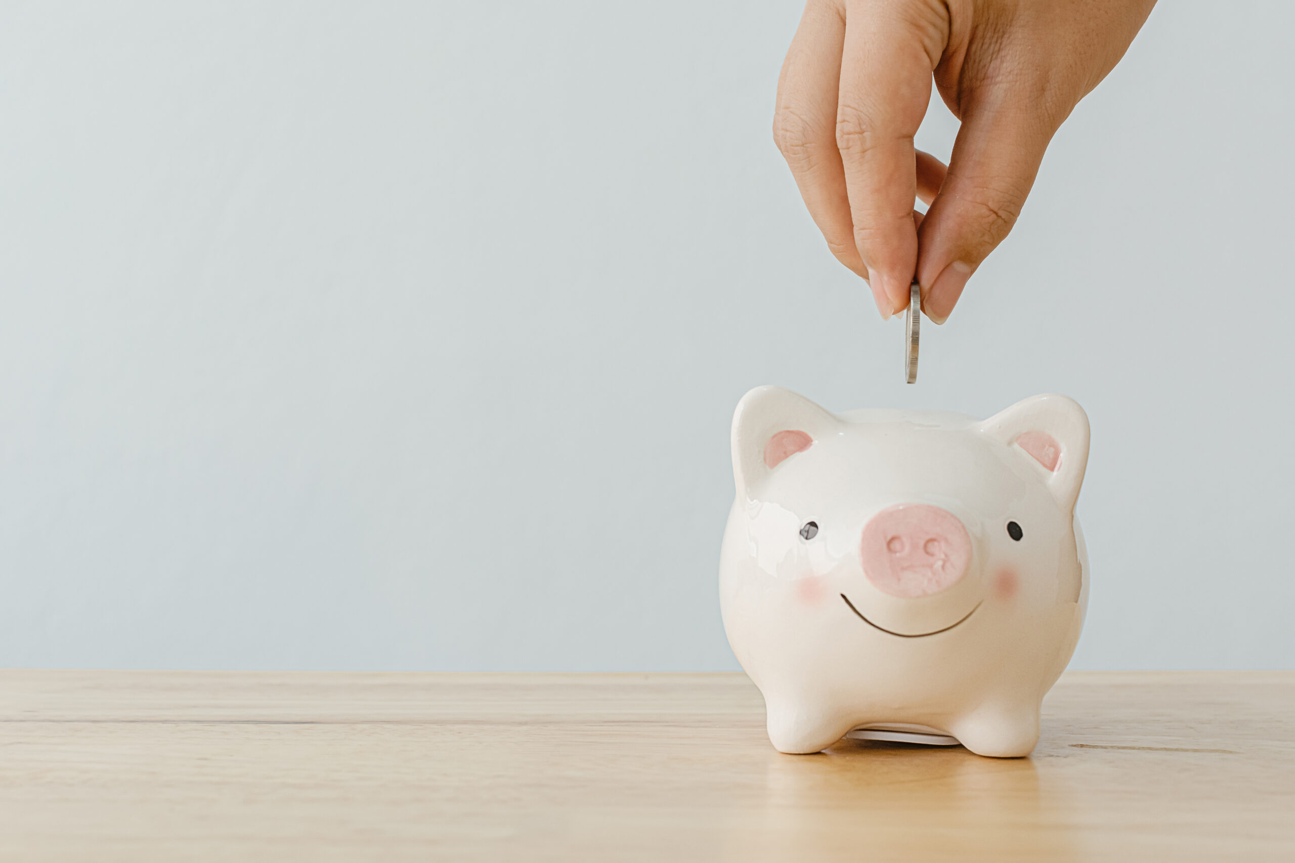 save money financial business investment. Hand of a man putting coins in piggy bank on wood table