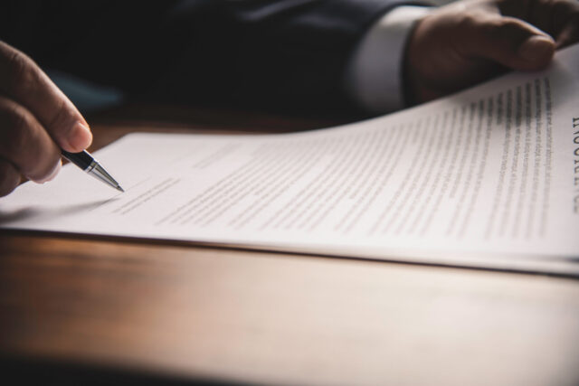 Hand holding pen signing contract in important documents.