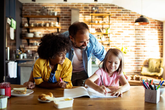 Father helping children with homework at kitchen table