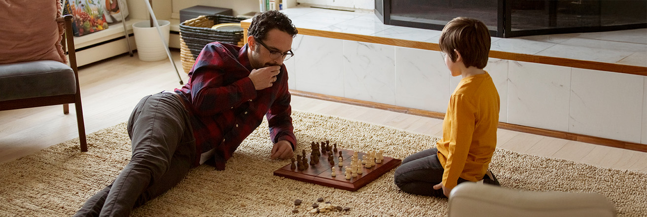 Son playing chess with father on carpet in living room at home