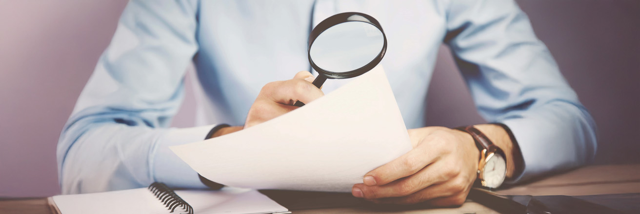 man holding magnifying glass examining document