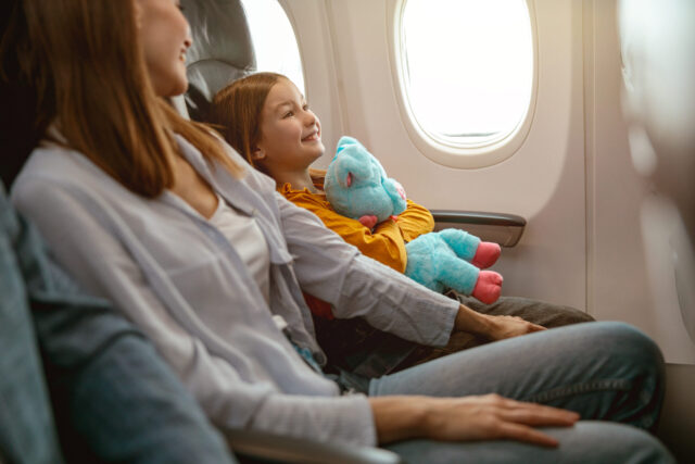 Joyful mother and daughter sitting in passenger airplane
