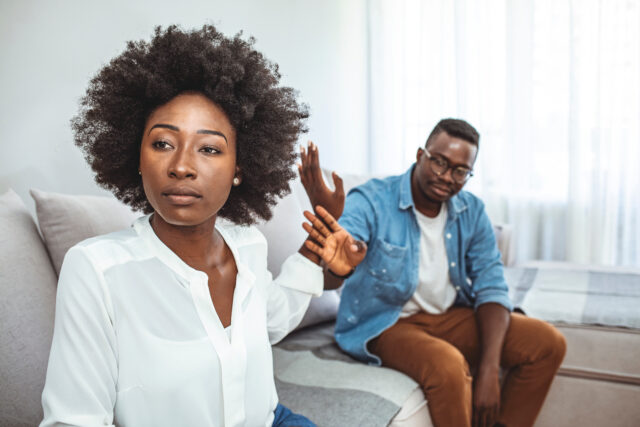 Unhappy young millennial married couple sitting on couch in living room after quarrel fight. Angry husband frustrated offended wife at home. Break up, divorce and misunderstanding in relations concept