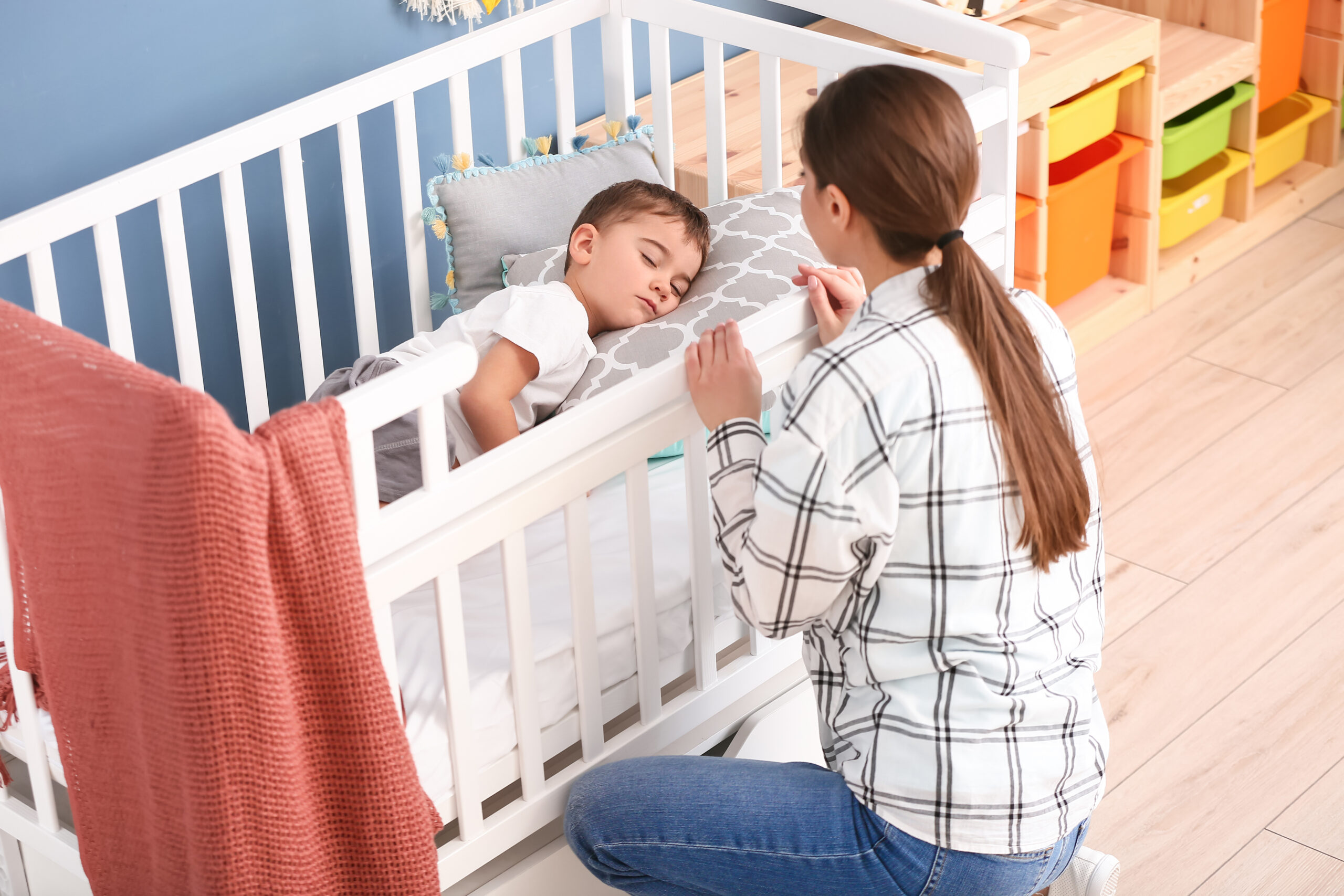 Nanny and cute little boy sleeping in crib at home